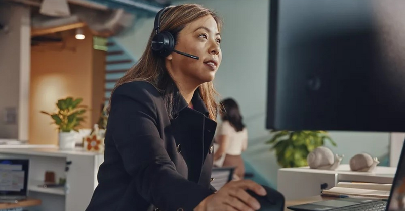 Professional woman wearing a headset and working on a computer during a virtual meeting in a modern office setting